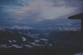 A panoramic view of snow-capped peaks from a glass-walled suite at dusk.