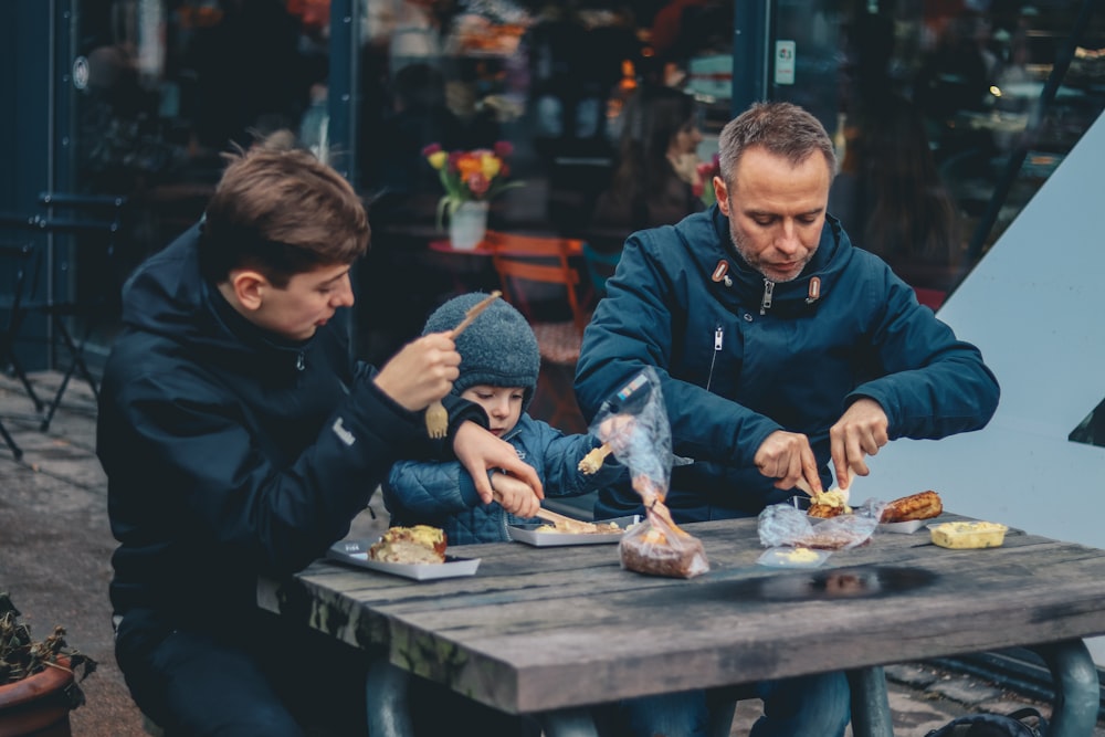 dos hombre y niño sentados frente a la mesa comiendo