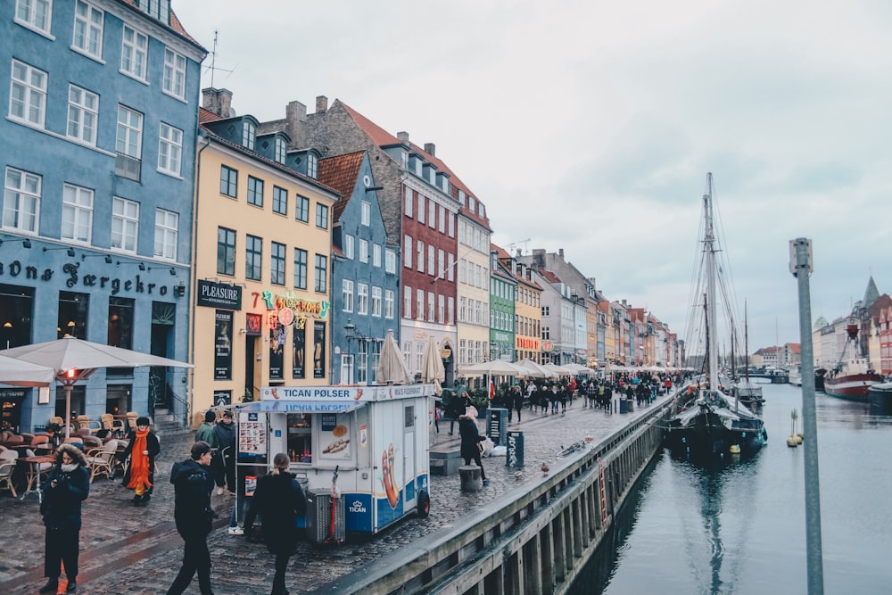 people walking in between of buildings and body of water