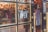 A storefront door with a glass window that has an 'OPEN' sign hanging on it. The door features gold-trimmed frames and ornate handles. Through the glass, a warmly lit interior is visible with hanging clothes and decorative lights.