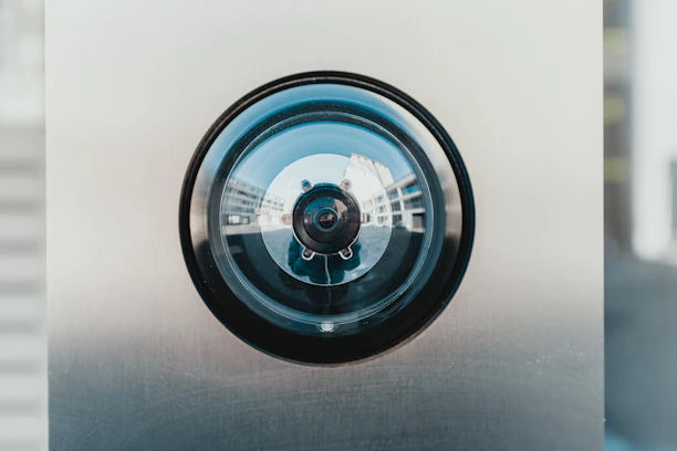 A close-up of a modern security camera lens reflecting a clear blue sky.