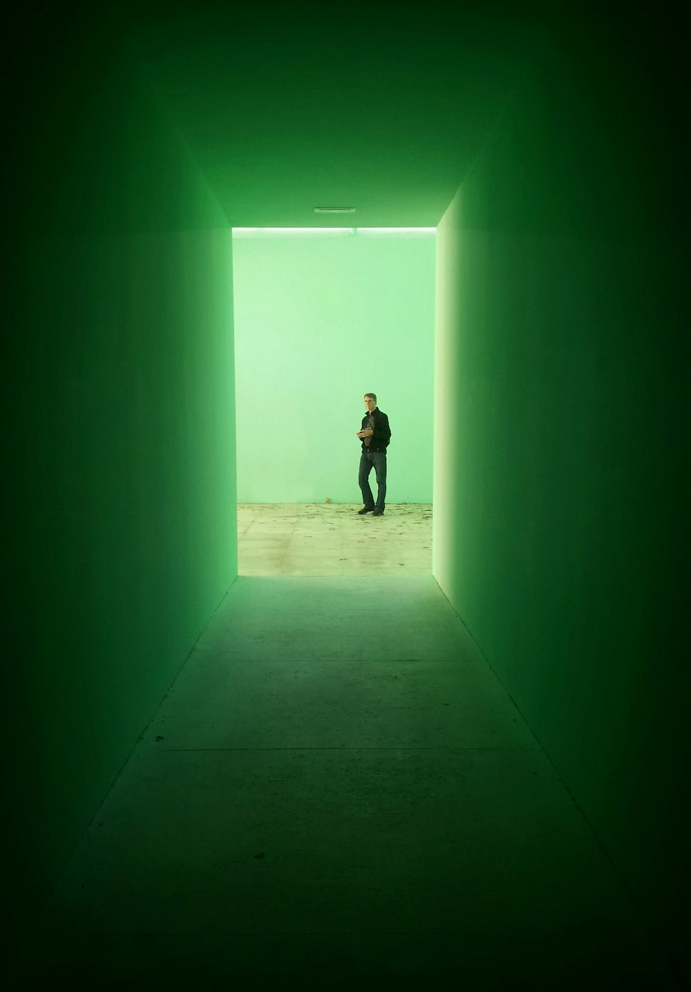 검은 재킷을 입은 남자가 녹색 벽 근처에 서 있습니다.