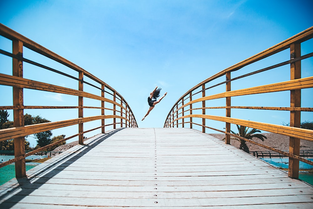 woman jumping near bridge during daytime