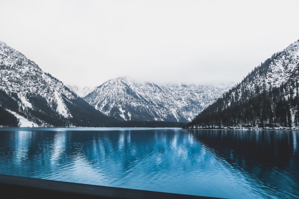 landscape photo of clear blue body of water near mountains covered with snow