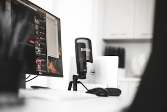 black Rode condenser microphone beside computer monitor