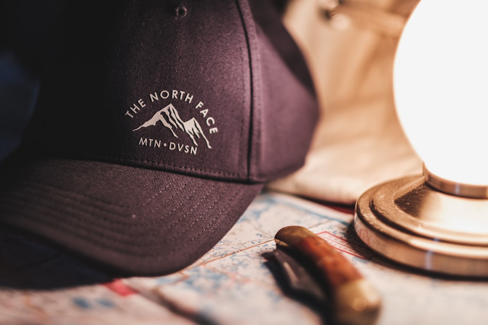 close-up photo of black and white The North Face cap beside brown pocket knife