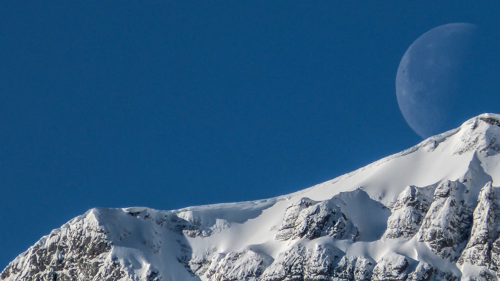 photo of full moon during daytime and ice coated mountain