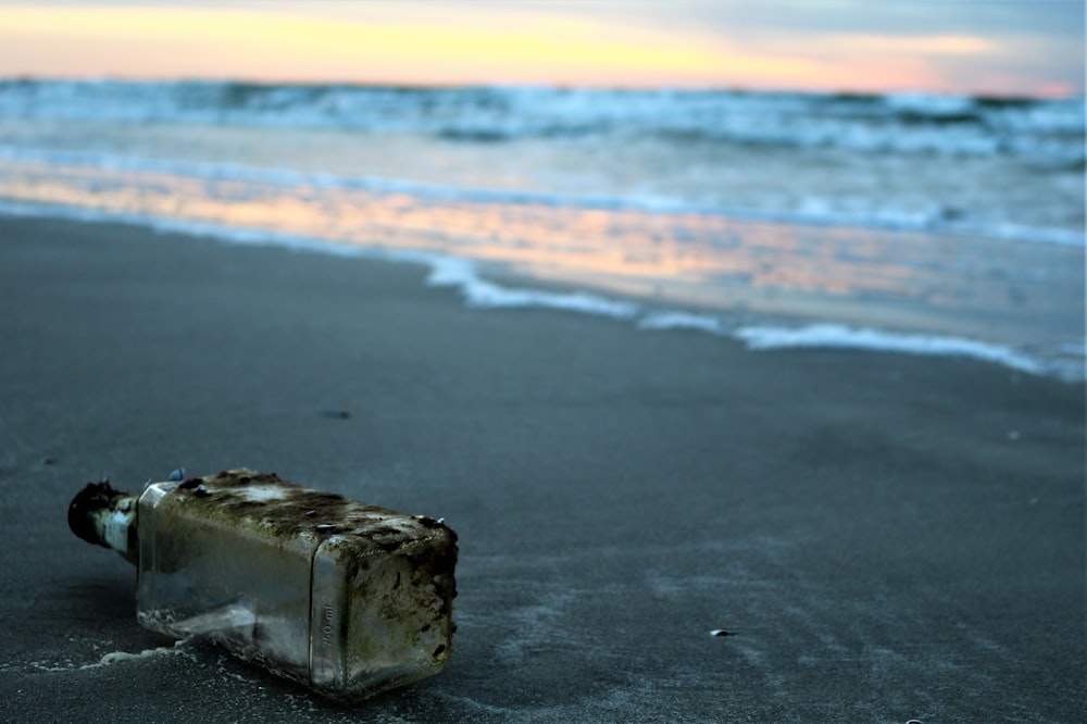 bottiglia di vetro in riva al mare vicino all'acqua di mare foto durante l'ora d'oro