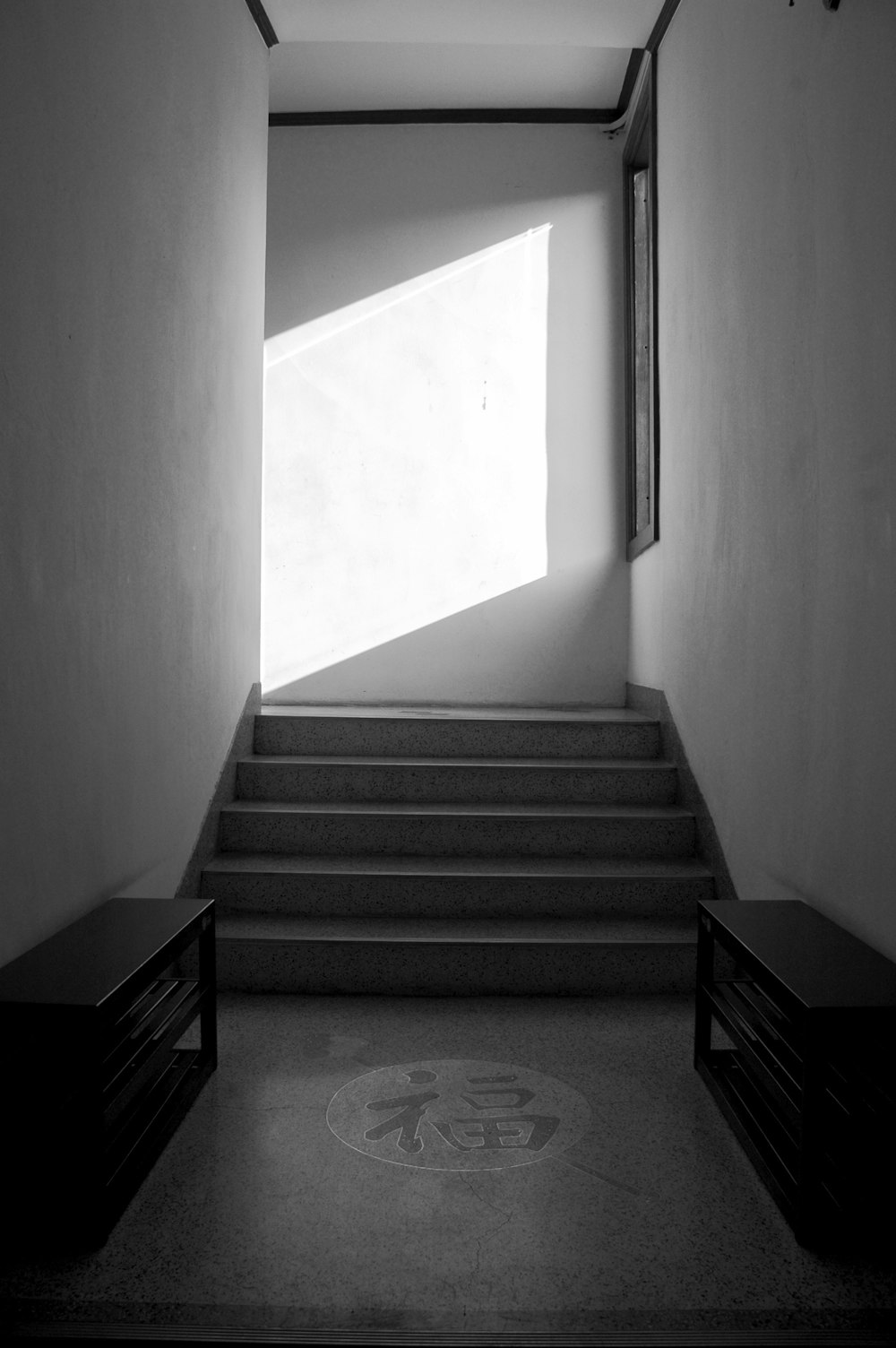 grayscale picture of two bench near kanji on floor and stairs