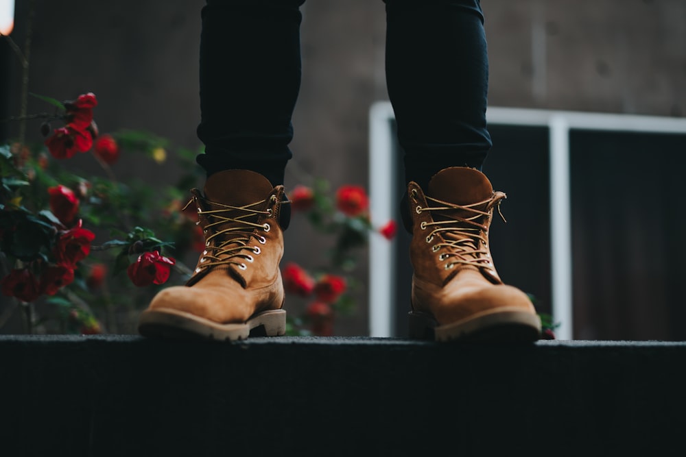 person wearing brown boots standing near red flowers