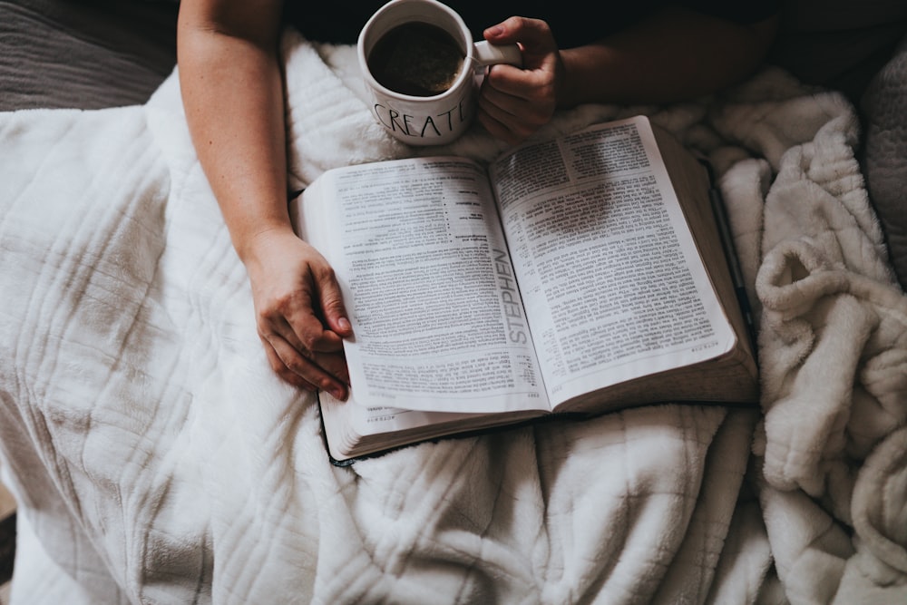 Person, die eine Tasse hält, während sie ein Buch liest