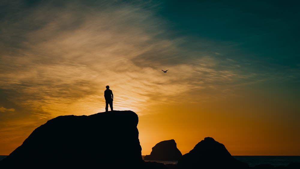 silhouette of man on cliff under blue sky during golden hour