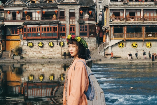 woman in pink dress standing in front of lake near temples in Fenghuang China