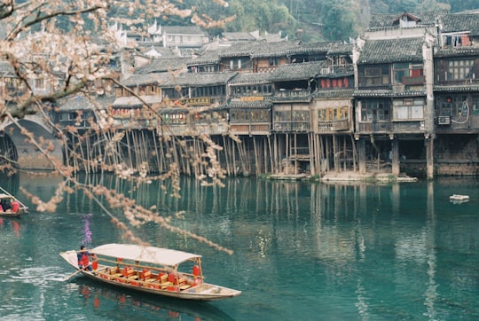 brown boat on body of water near buildings in Fenghuang China