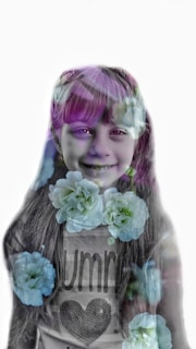 A portrait of a young girl smiling, with an overlay of large, white flowers across the image, creating a dreamy and whimsical effect. The girl's long hair and casual shirt with a heart design are partially visible.