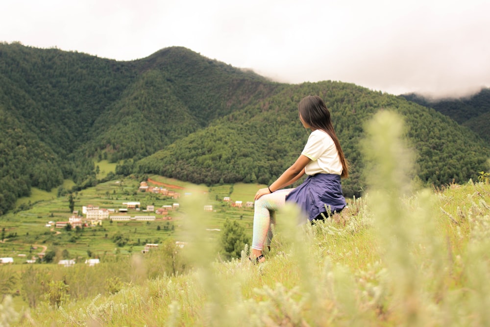 Frau sitzt tagsüber auf einem Hügel, der mit grünem Gras bedeckt ist