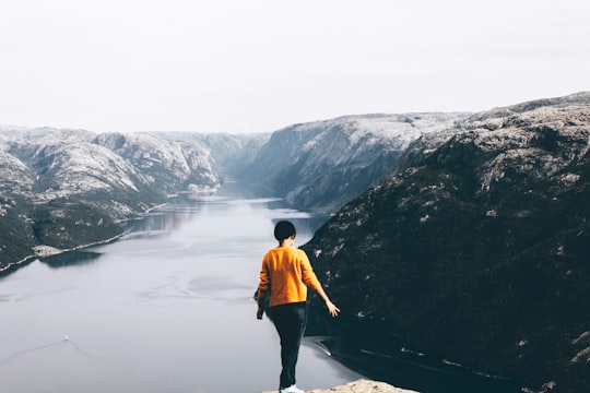 standing woman on cliff with overlooking of mountain and body of water in Stavanger Norway