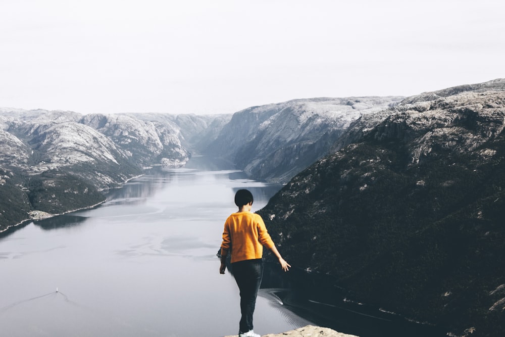 standing woman on cliff with overlooking of mountain and body of water