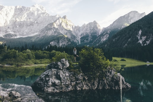 A serene landscape with a person meditating by a calm lake at sunrise.