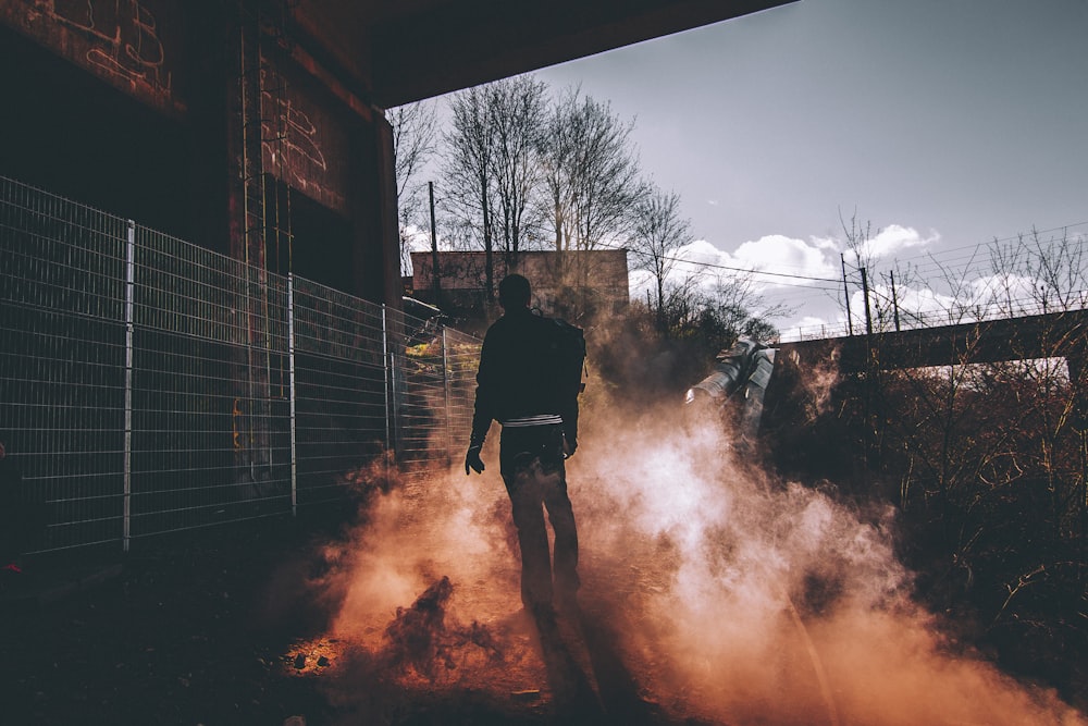 man wearing black jacket and black pants standing near wire fence