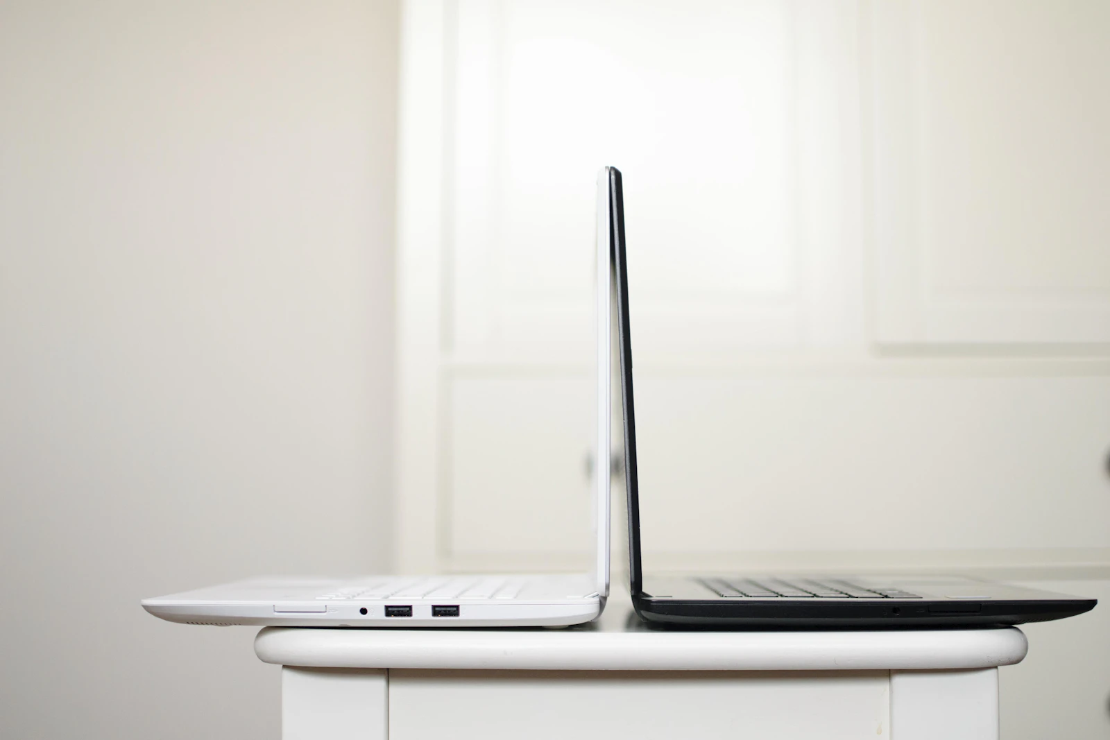 Two open laptops side by side on a desk with a coffee mug