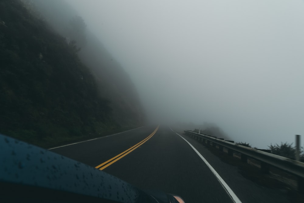 black asphalt road between green trees covered with fog during daytime