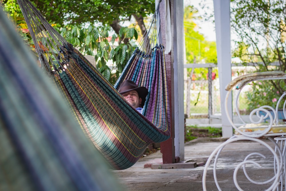 man laying down on multicolored hammock hanged on porch column