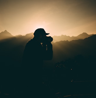 silhouette of man carrying camera near mountains during sunset