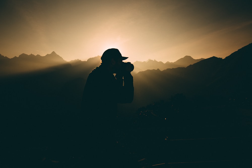 silhouette of man carrying camera near mountains during sunset