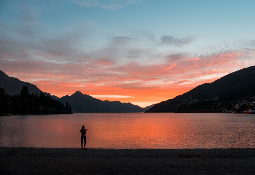 silhouette photo of woman standing while facing body of water