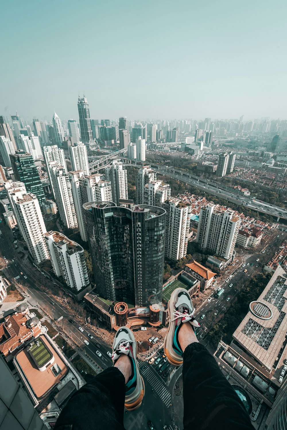 aerial photography of person wearing low-top sneakers over high rise concrete building at daytime