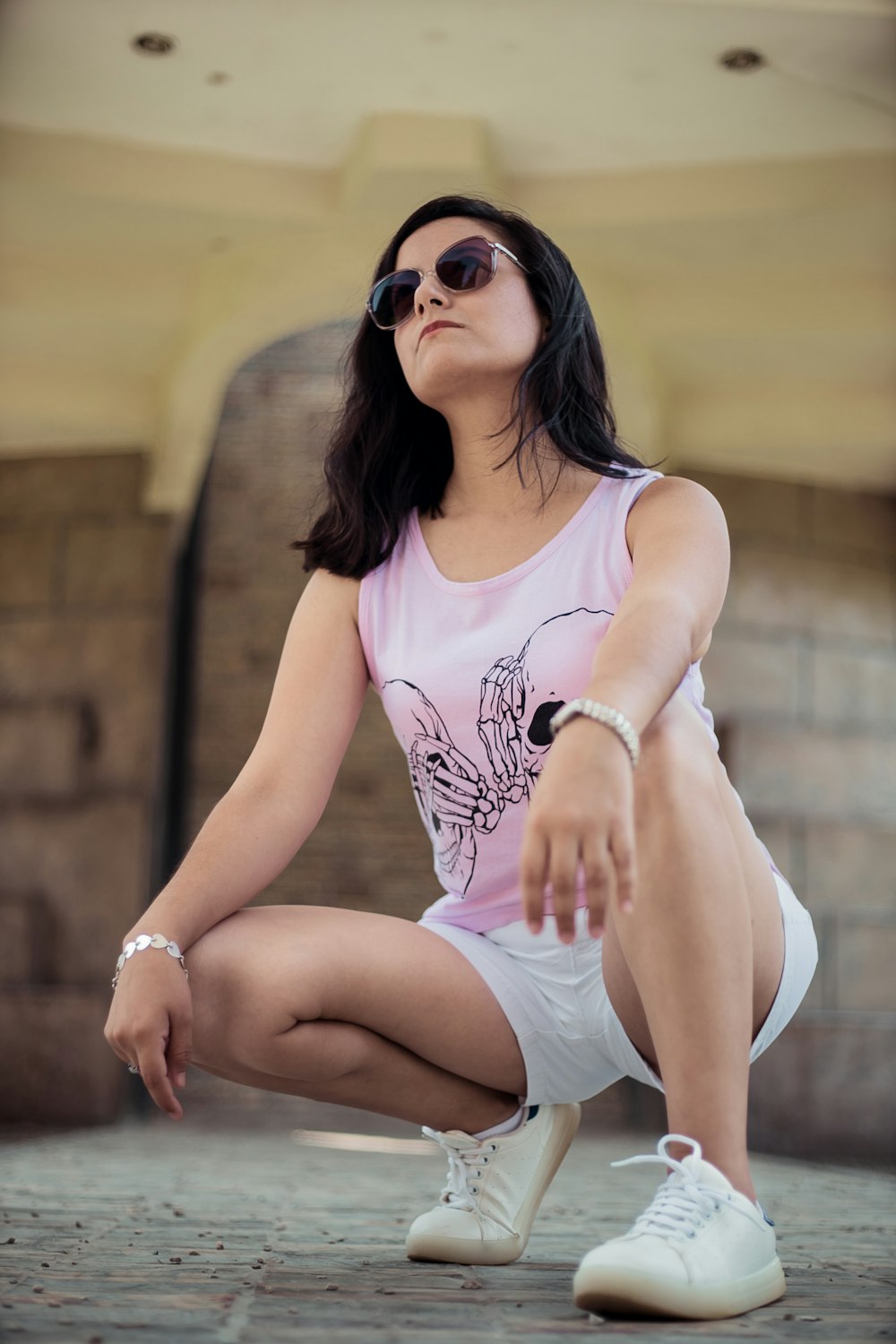 woman in pink tank and white shorts taking photo near brown concrete wall