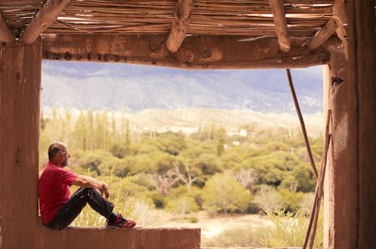 person sitting on concrete rail near green grass during daytime in Amaicha del Valle Argentina