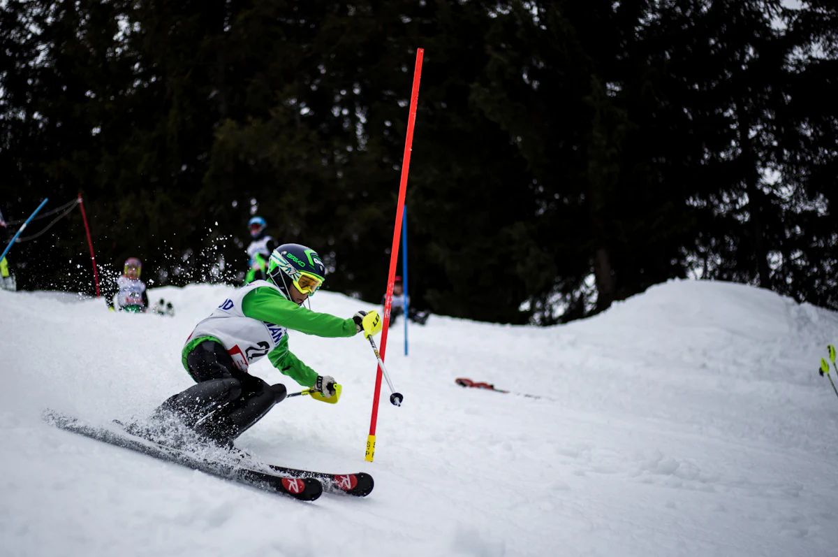 A slalom racer leans past a gate on a race course lined with pines