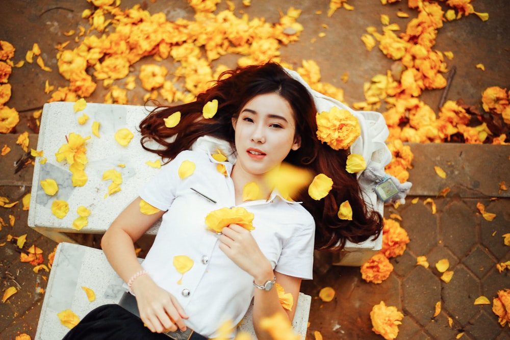 uma mulher deitada em um banco cercado por flores amarelas