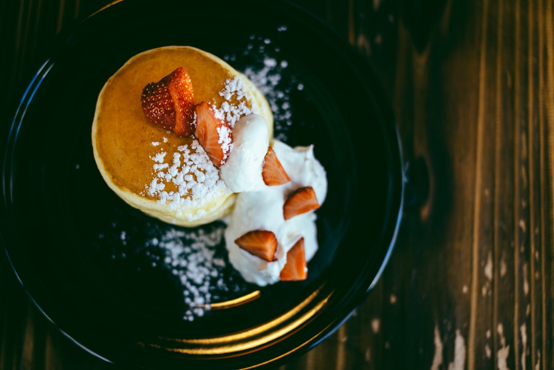 strawberry topped pancake with whip cream on round black ceramic plate