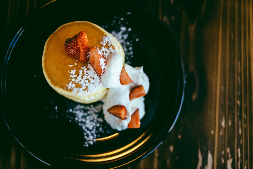 strawberry topped pancake with whip cream on round black ceramic plate
