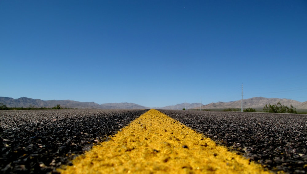 photo of black and yellow asphalt road under clear blue sky during daytime