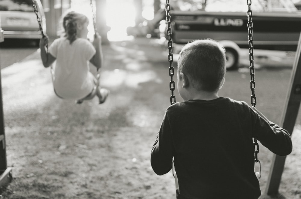 grayscale photography of boy and girl on swing
