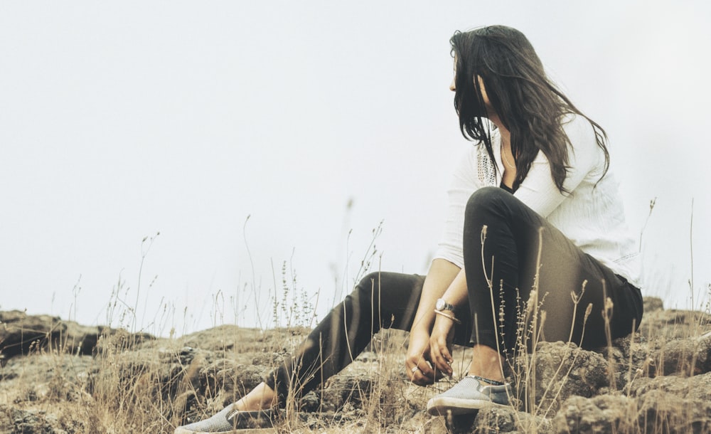 selective focus photography of woman in white long-sleeved shirt sitting on gray rock