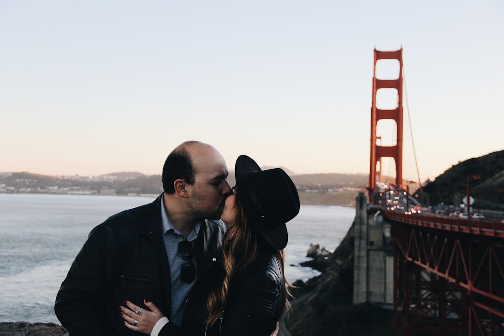 man and woman kissing beside Golden Gate Bridge during daytime