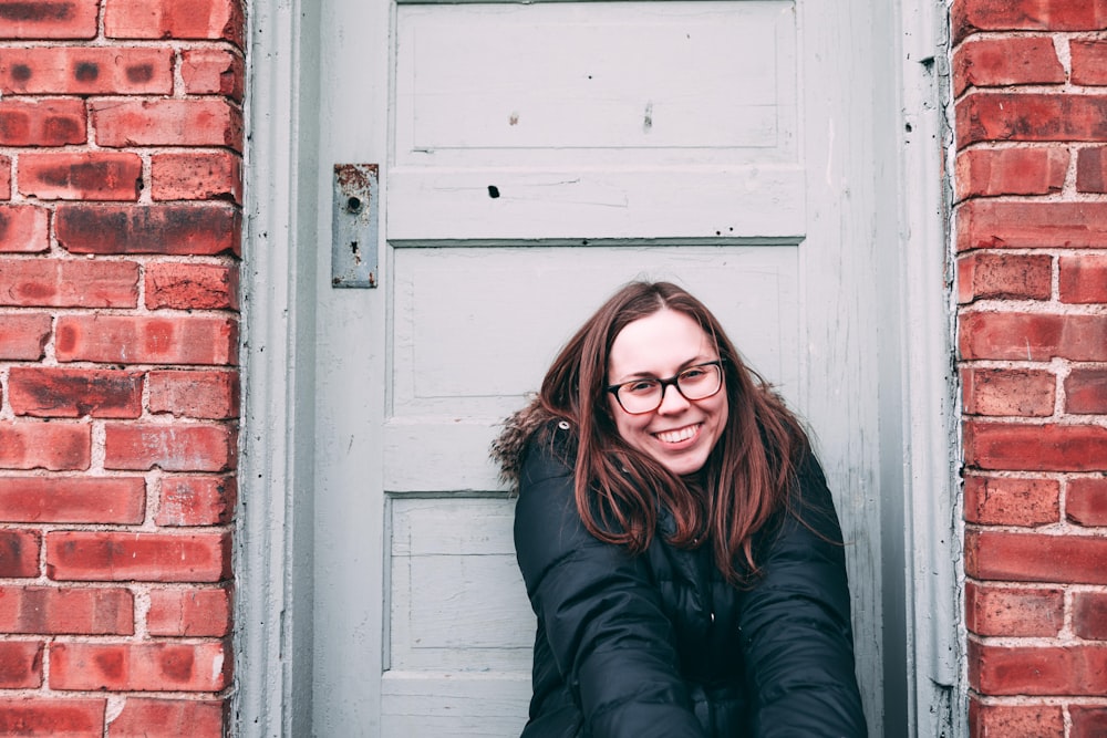 smiling woman sits beside white wooden door during daytime