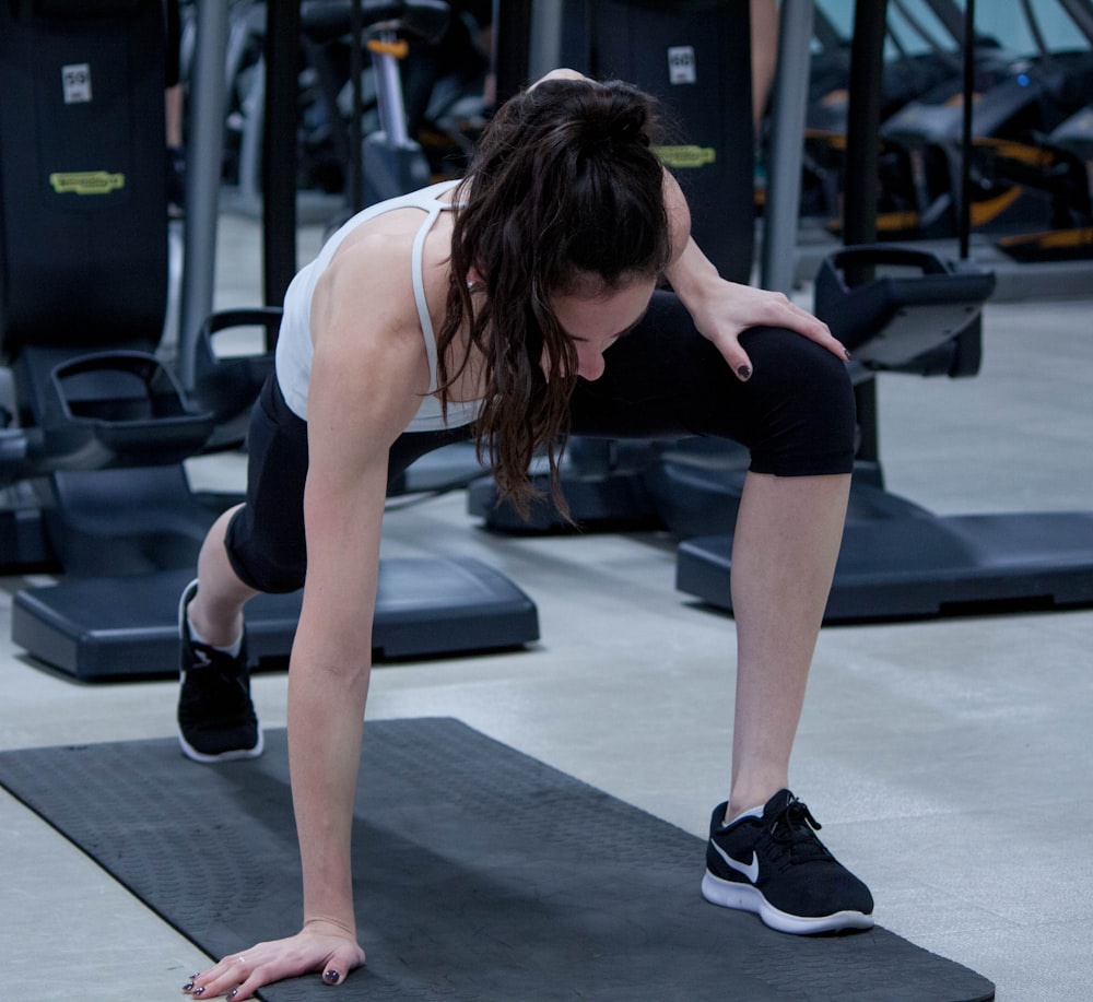 femme étirant les jambes et les bras sur un tapis de yoga noir