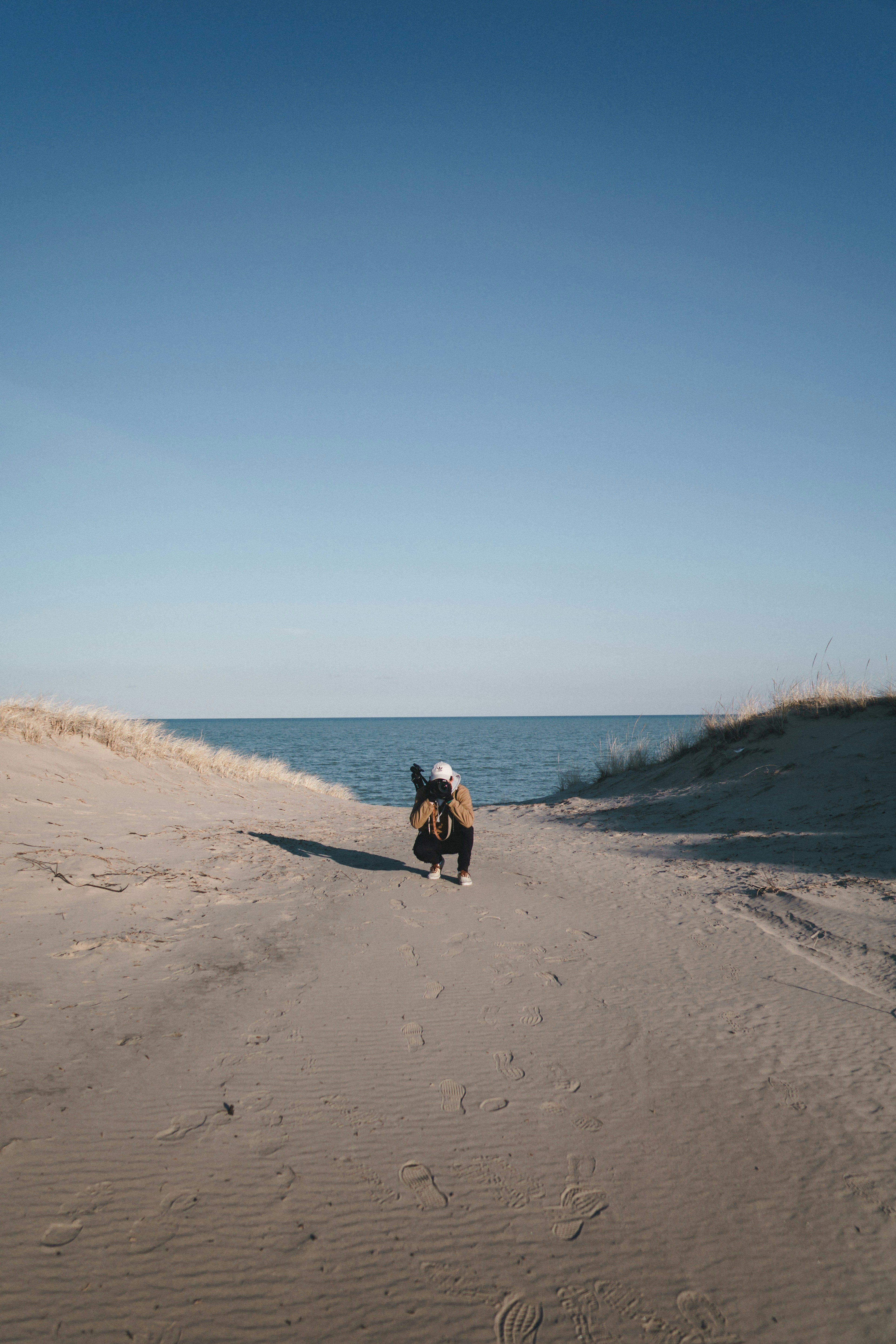 person sits on sand across body of water