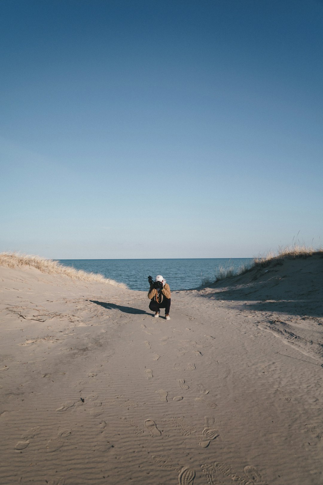 person sits on sand across body of water