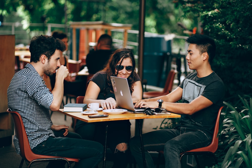 Three people sitting and talking whilst working on a laptop and drinking coffee