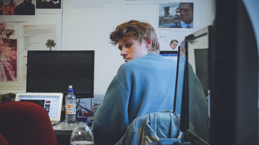 man wearing blue top sitting in front of computer