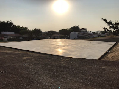 Workers smoothing a large concrete slab under a bright orange sky.