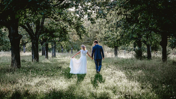 bride and groom walking on grass field between treeline photo