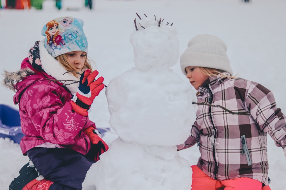 two girl molding a snowman during daytime